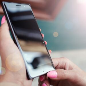Home Close-up of hands holding a smartphone outdoors with a bright lens flare and reflections.